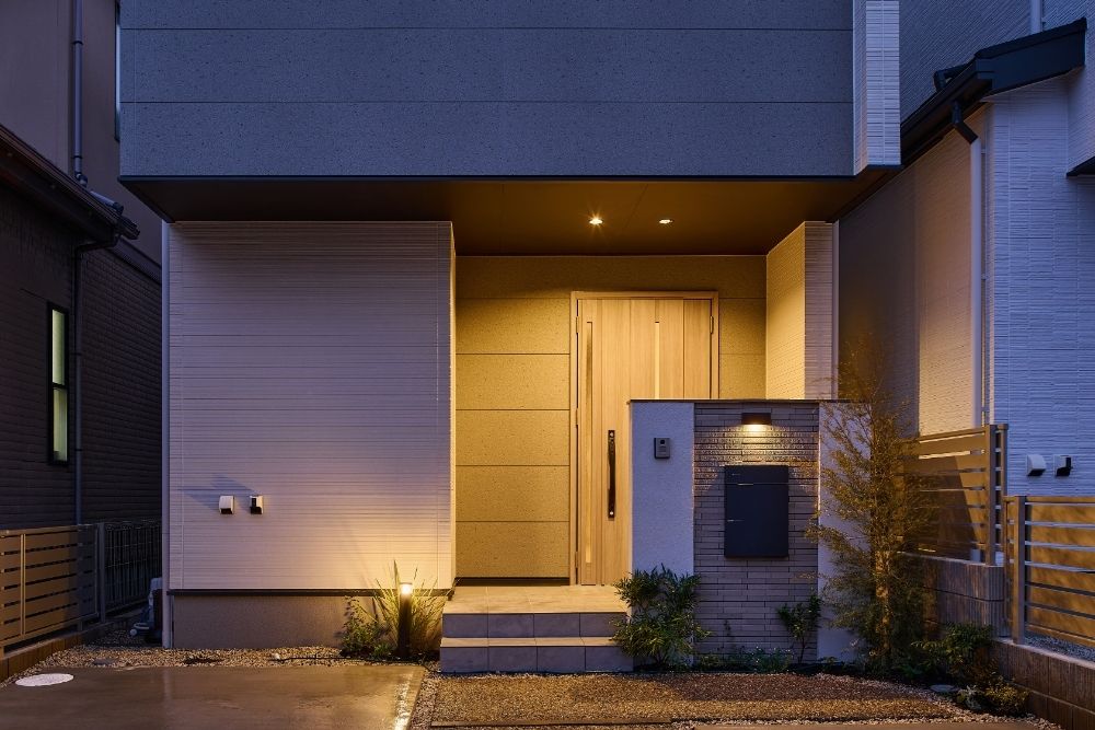 夜の玄関アプローチを温かく照らすセンサーライトと、視線を遮る袖壁を設けた防犯性の高い注文住宅の外観。