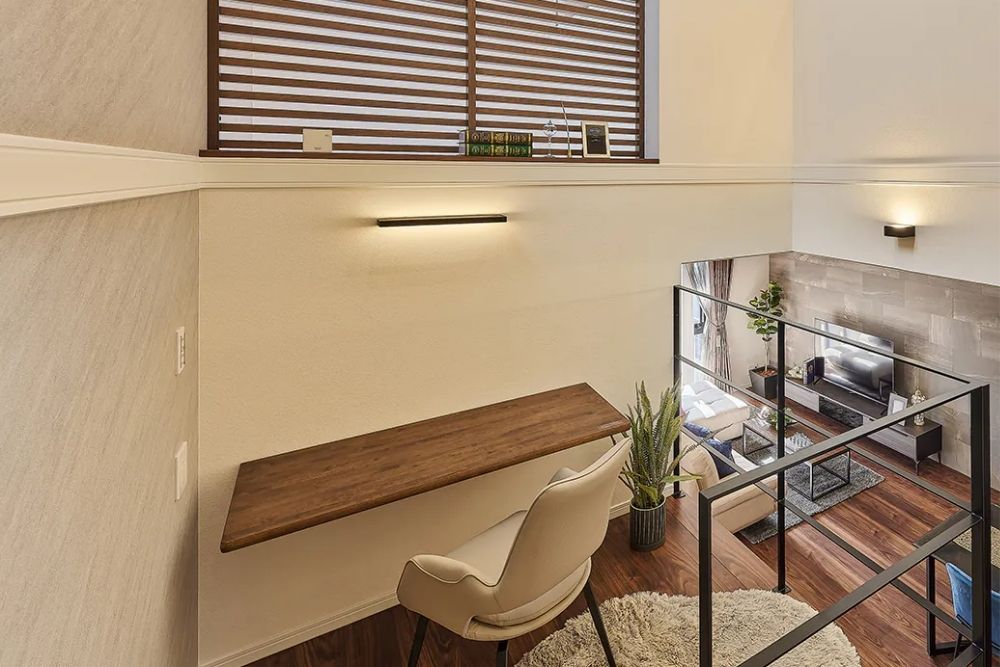 吹抜け空間に面したスキップフロアのワークスペース。デスクからはリビングダイニングを見下ろせ、高い窓から光が差し込む開放的な注文住宅の内装。