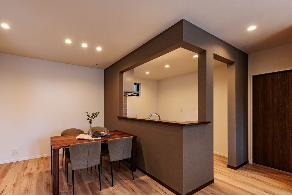 注文住宅の独立キッチン。白を基調とした清潔感のあるシステムキッチンと、木目調の吊り戸棚、落ち着いたグレーのタイル壁が特徴的なキッチン空間。